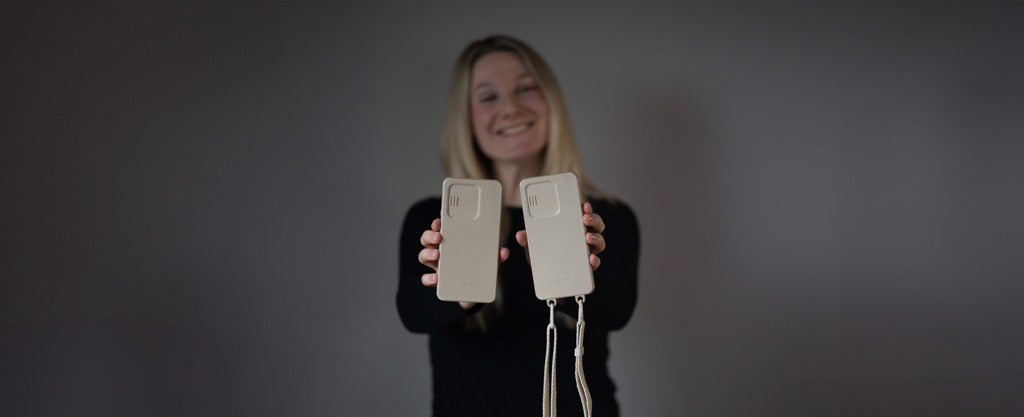 Frau hält Closd Handyhülle mit Kameraschutz in beige einmal mit und einmal ohne Handyband vor grauem Hintergrund