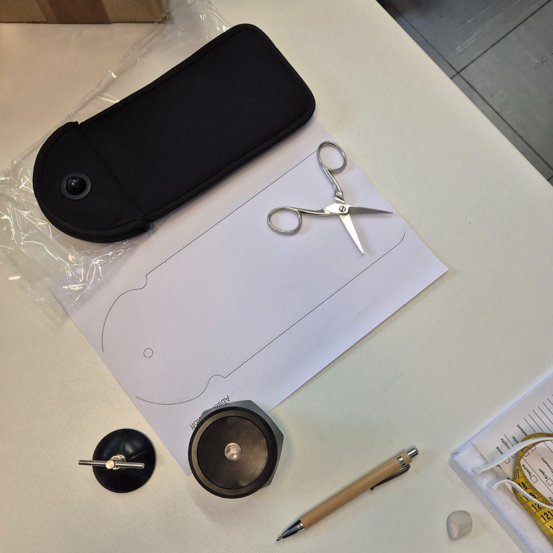 Closd Handytasche liegt auf einem Schneidertisch mit einer Schere und einem Maßband und einem mobilen Öffnungsmagnet